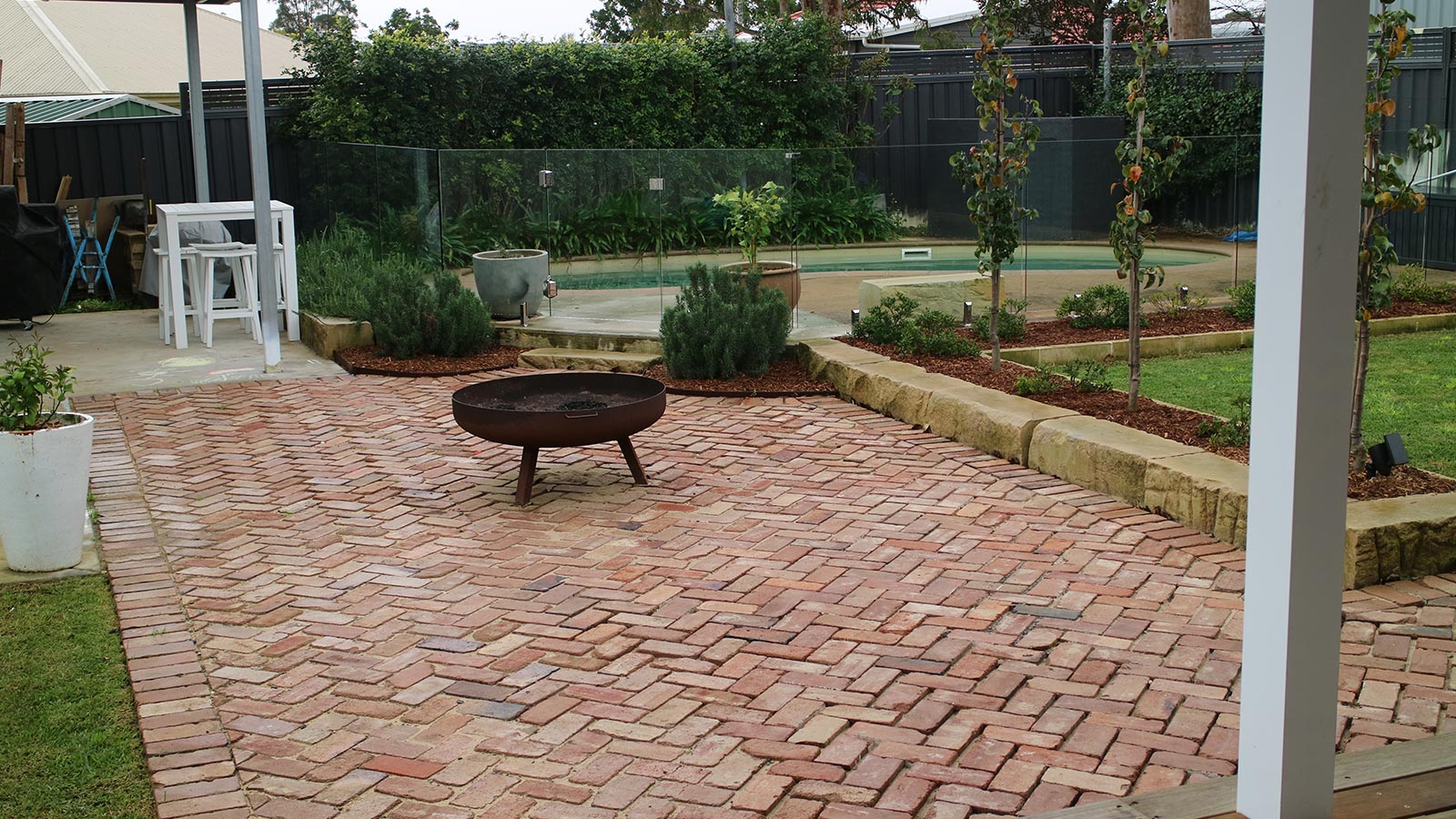 Medowie backyard after the brick entertaining area, fire pit, garden beds and glass pool fence were completed
